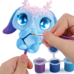 Osoba używa małego pędzla do namalowania Figurki do malowania z Agathą - uroczego stworzenia z dużymi niebieskimi oczami, różowym porożem i długimi uszami. Trzy otwarte pojemniki z farbą (niebieski, fioletowy, biały) znajdują się poniżej na białym tle.