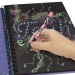 Ręka używa Zestawu długopisów żelowych w neonowych kolorach, aby narysować "Wiarę" w pastelowych i neonowych kolorach z kwiatowymi detalami na czarnym papierze w spiralnym notatniku; fioletowa kartka wystaje, dodając żywy, artystyczny akcent.