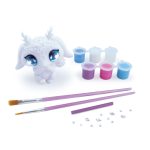 Biała, niepomalowana figurka do malowania z Agathą z dużymi niebieskimi oczami siedzi obok niebieskich, fioletowych i białych naczyń z farbą, dwóch pędzli, fioletowego narzędzia do rzeźbienia oraz rozsypanych dżetów i klejnotów na białym tle.